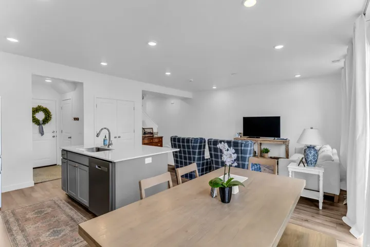 Kitchen island with a white countertop and integrated sink, stainless steel dishwasher, wood-finish flooring, recessed lighting, and white walls