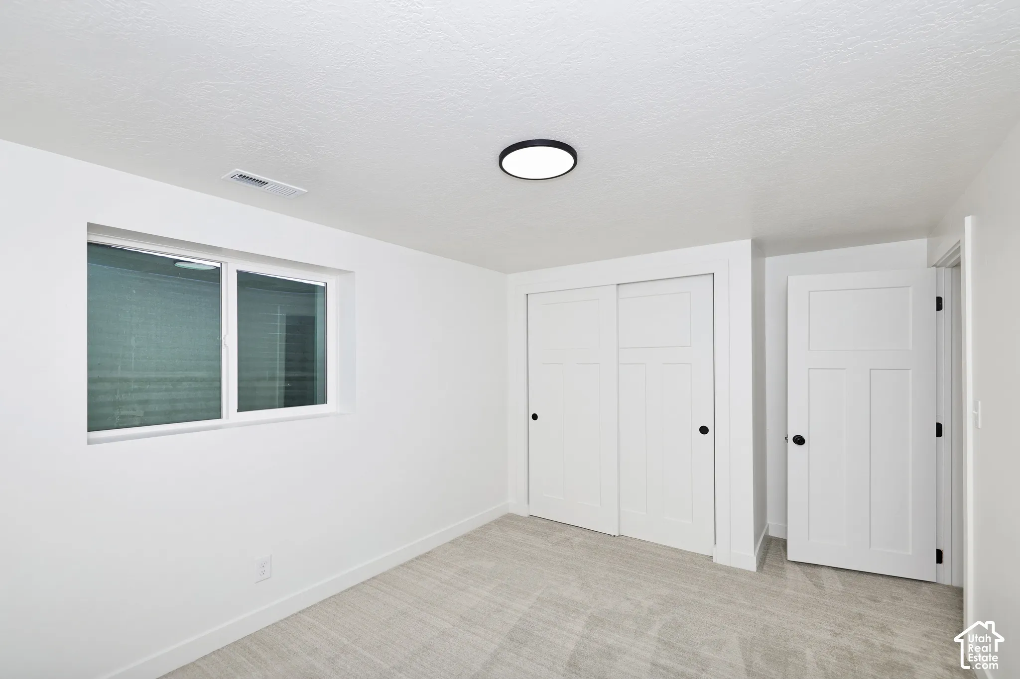Neutral tone carpeting, white walls, modern ceiling light fixture, white framed window, and white interior doors with black hardware