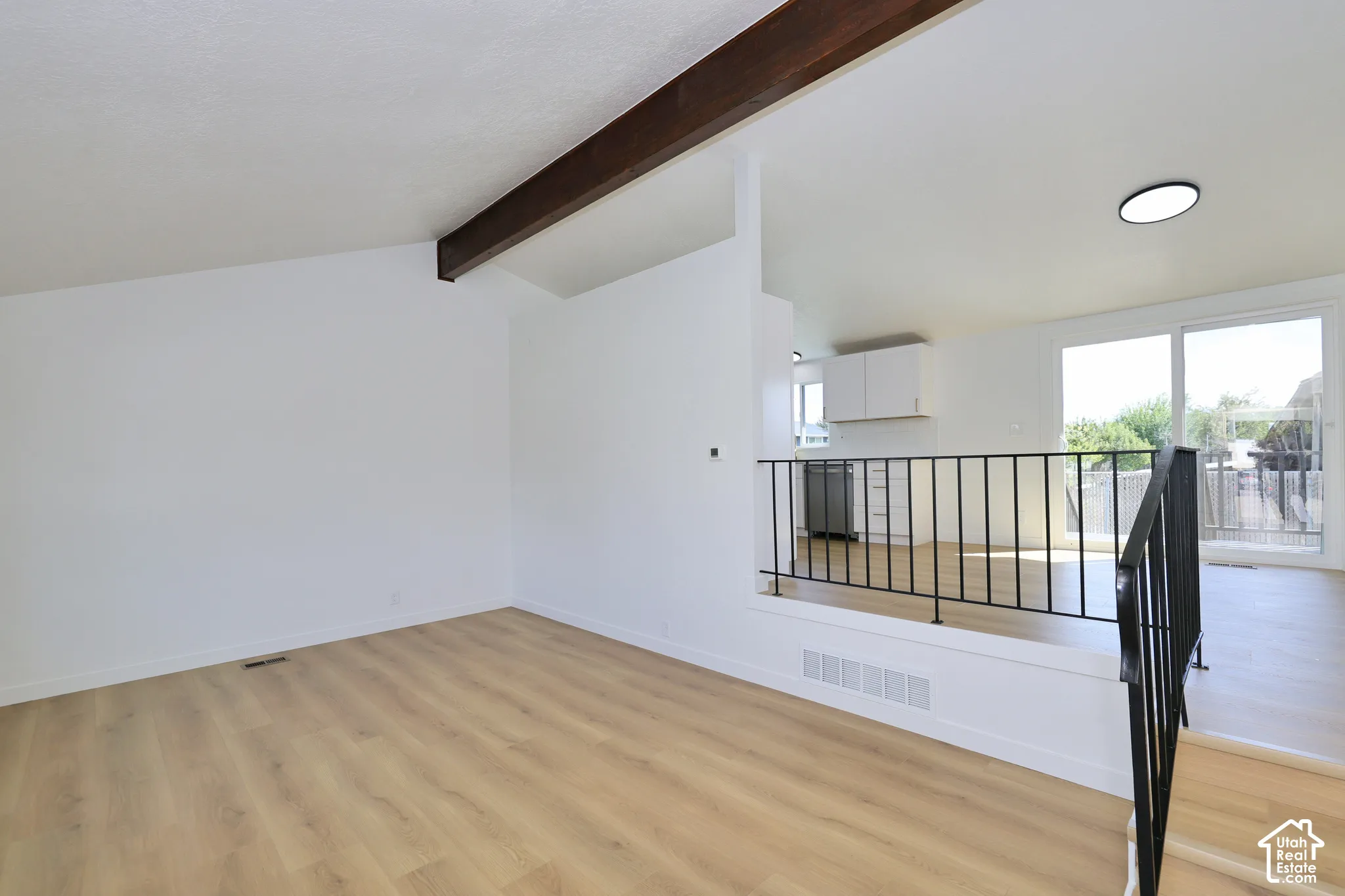 Vaulted ceiling with exposed wood beam, wood-finish flooring, sliding glass door, white cabinetry, and black metal railing
