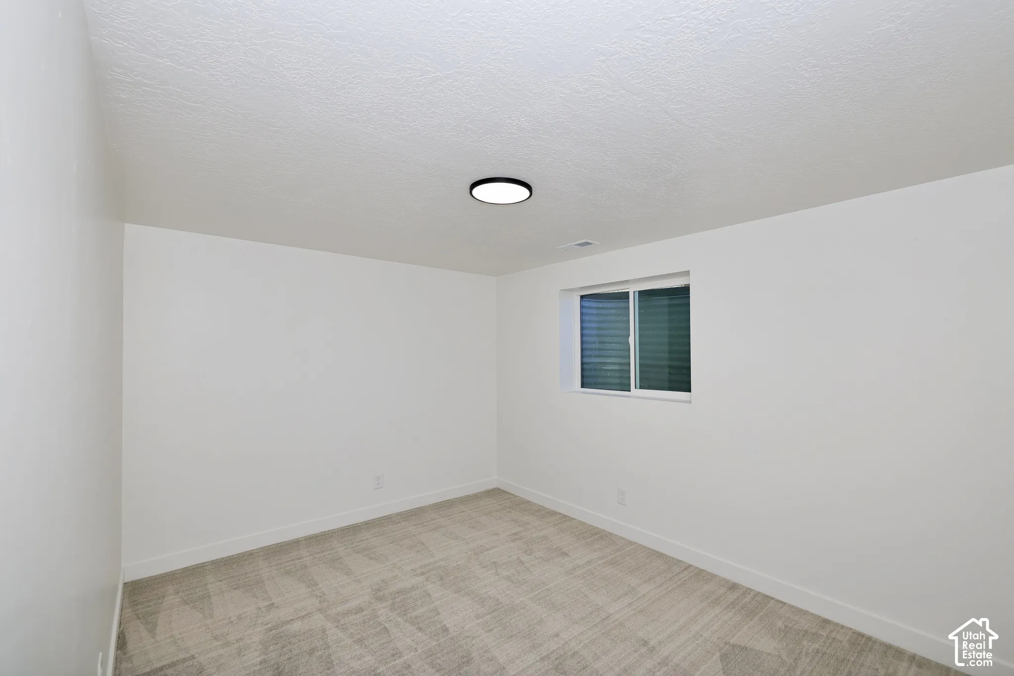 Carpeted flooring, white walls, and a single window with blinds