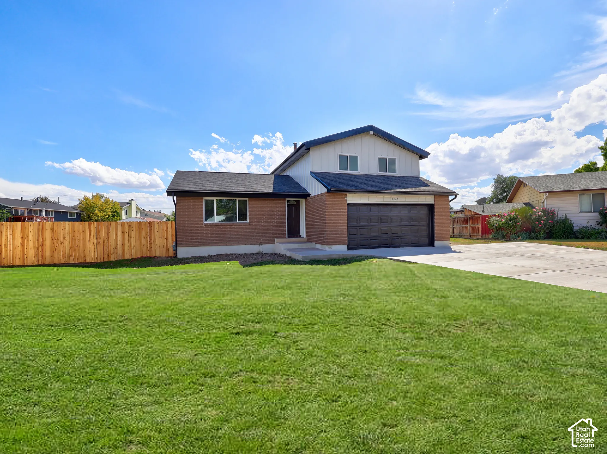 Brick and siding exterior, attached garage, concrete driveway, front lawn, and wood privacy fence