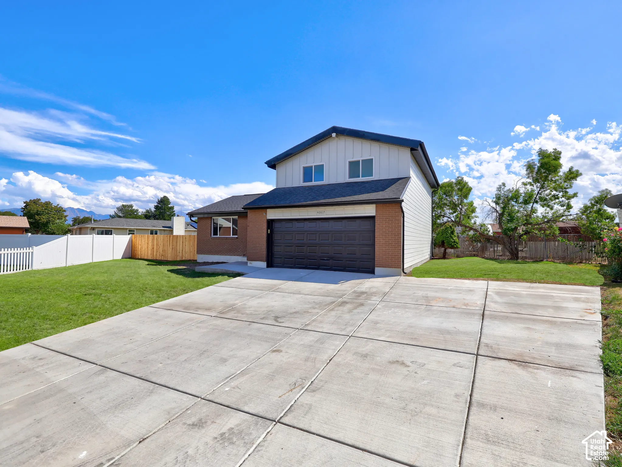 Brick and siding exterior with a dark garage door, concrete driveway, and landscaped front lawn