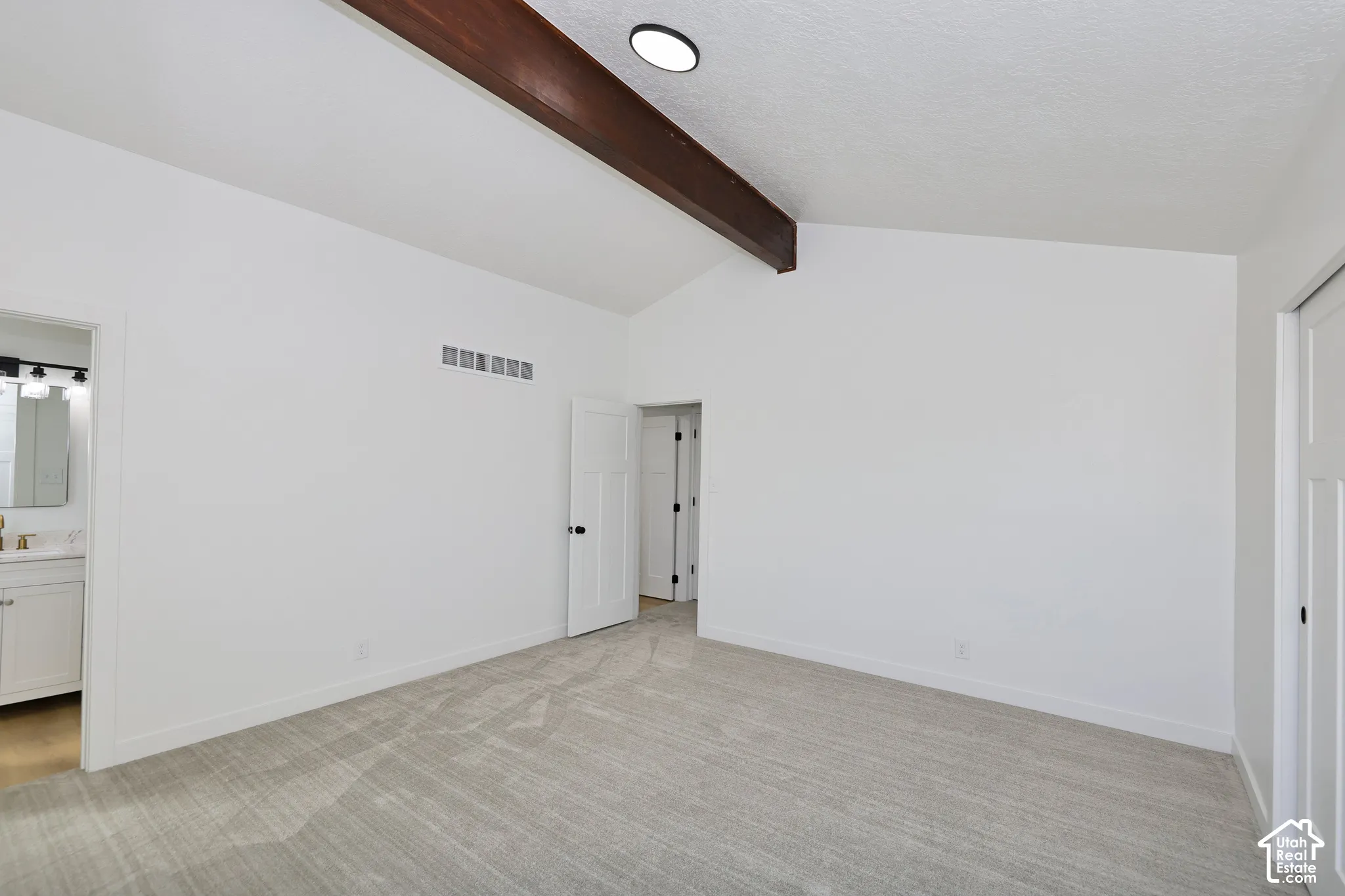 Vaulted ceiling with an exposed wood beam, recessed lighting, neutral tone carpet, and a paneled interior door