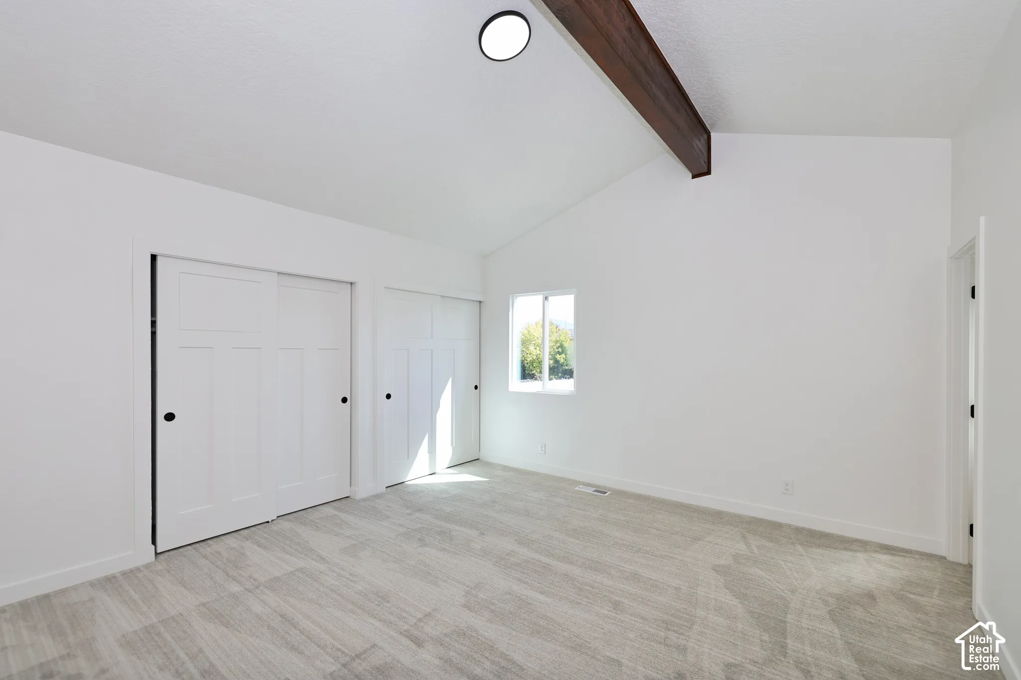 Vaulted white ceiling with exposed wood beam, two panel-style sliding closet doors, and recessed lighting