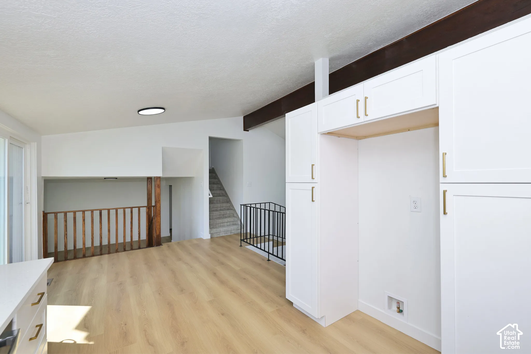 White shaker cabinetry with gold-finish hardware, wood-finish flooring, and exposed ceiling beams