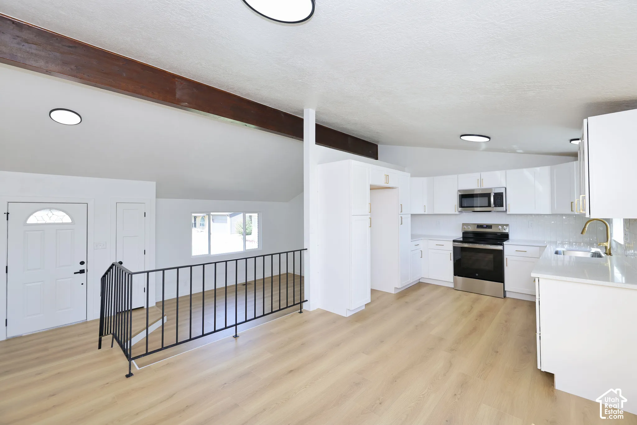 Modern kitchen with white cabinetry, stainless steel appliances, and a light-toned wood-finish floor