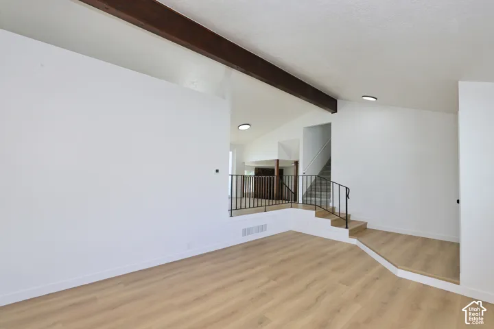 Vaulted ceiling with exposed wood beams, wood-finish flooring, white walls, and a black metal railing