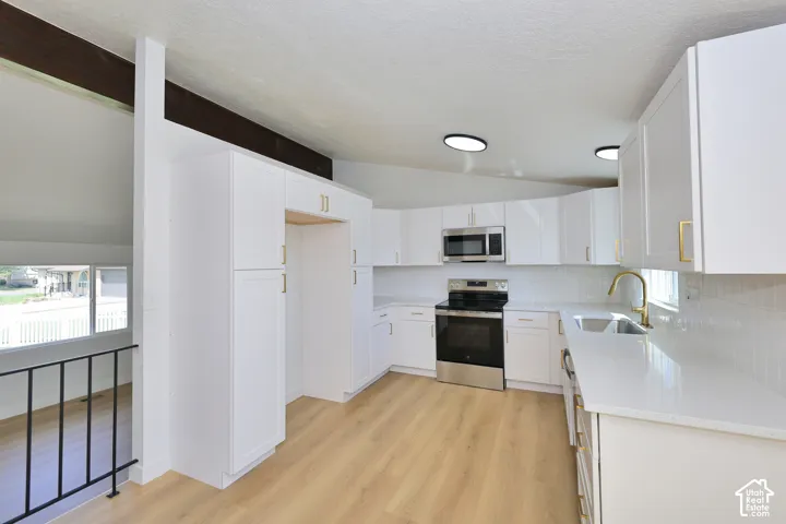 Kitchen with white cabinetry, stainless steel appliances, light-toned wood-finish flooring, and white countertops
