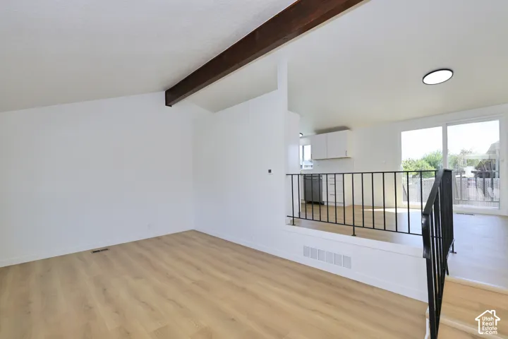 Vaulted ceiling with exposed wood beam, wood-finish flooring, sliding glass door, white cabinetry, and black metal railing
