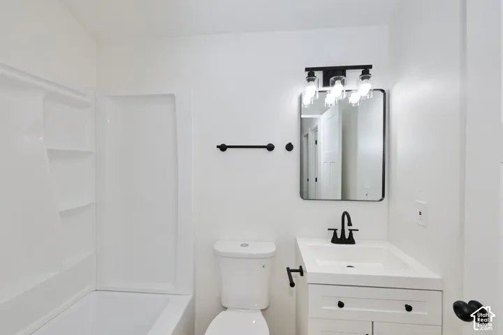 White bathtub with integrated shelving, matte black vanity light fixture, rectangular mirror with a black frame, white vanity with black hardware, and a black faucet