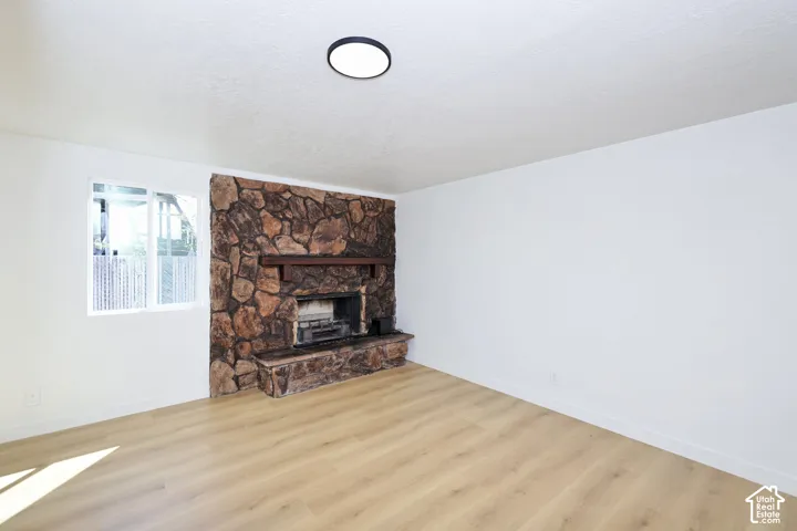 Stone fireplace with wood mantel, wood-finish flooring, white walls, and a recessed ceiling light