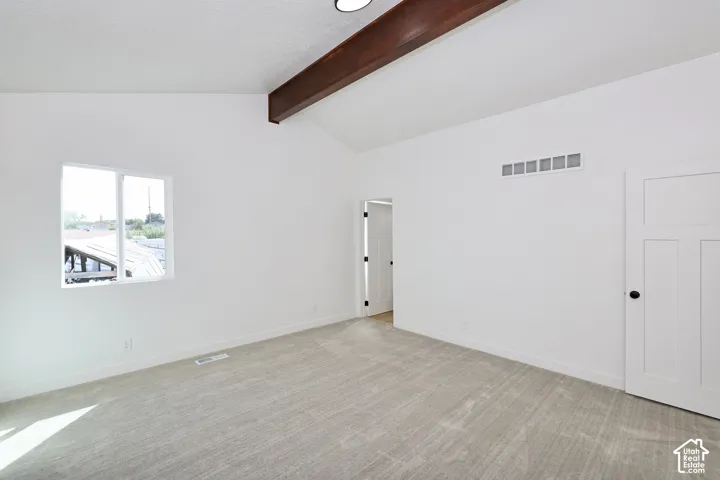 Vaulted ceiling featuring an exposed beam, light gray carpet, white interior door with black hardware, and a single window