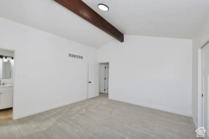 Vaulted ceiling with an exposed wood beam, recessed lighting, neutral tone carpet, and a paneled interior door