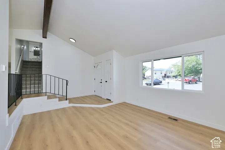 Vaulted ceiling with an exposed wood beam, wood-finish flooring, a contemporary window, and a white paneled entry door