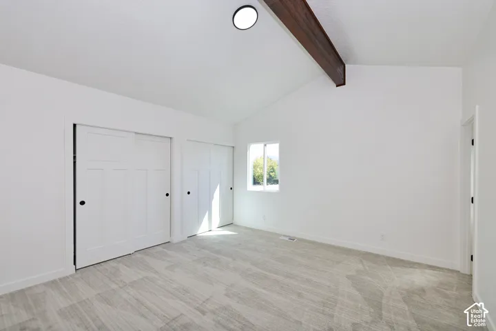 Vaulted white ceiling with exposed wood beam, two panel-style sliding closet doors, and recessed lighting