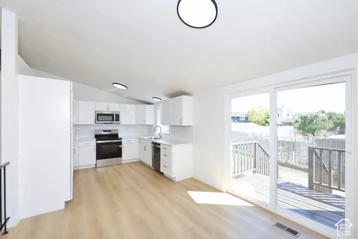 Modern kitchen with white shaker cabinetry, stainless steel appliances, and wood-finish flooring