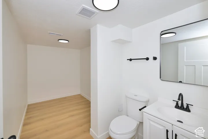 White vanity with an integrated sink and matte black faucet, rectangular wall-mounted mirror, and wood-finish flooring