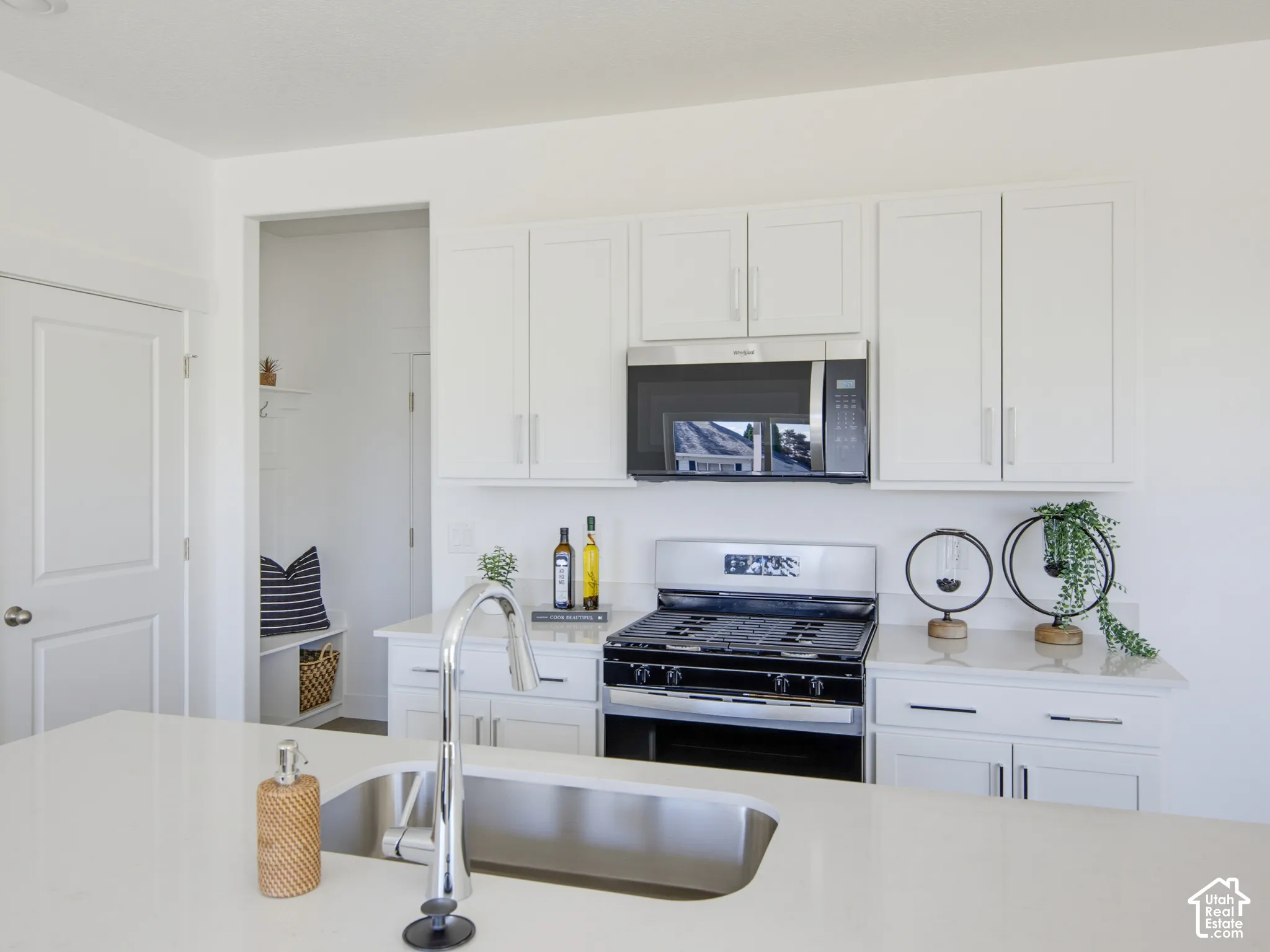 Kitchen featuring white cabinetry, quartz countertops, stainless steel undermount sink with a high-arch faucet, and built-in stainless steel appliances
