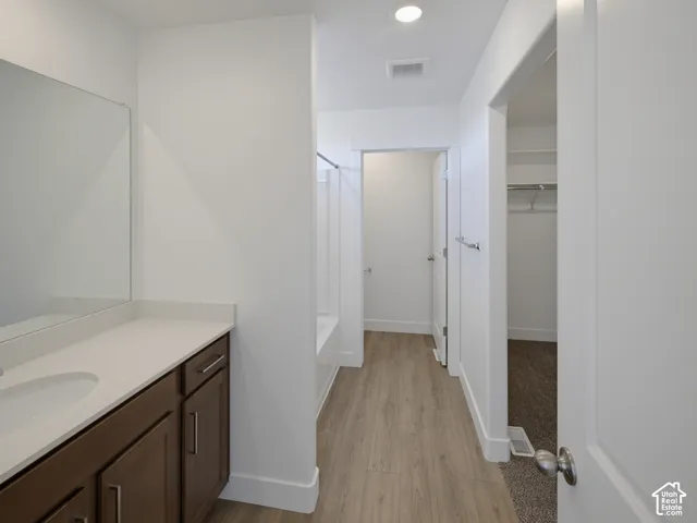 Contemporary bathroom featuring a wood-finish vanity with a single sink and light-toned countertop, a shower-tub combination, and wood-finish flooring