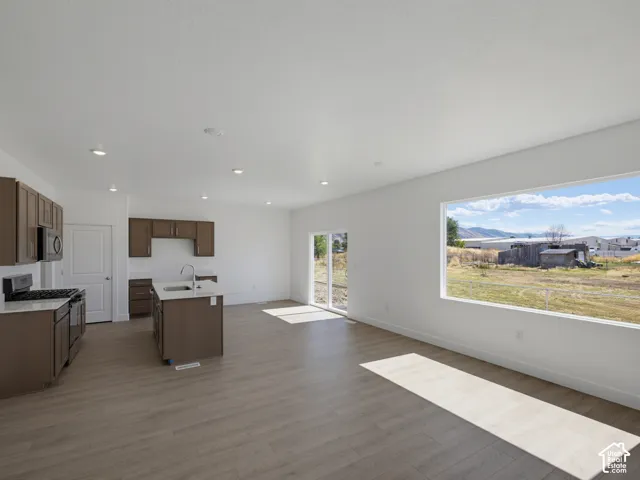 Open concept living space featuring wood-finish flooring, a kitchen island with sink, recessed lighting, and a large picture window
