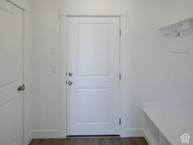 White shaker-style door with brushed nickel hardware, wood-finish flooring, and a built-in storage bench with coat hooks