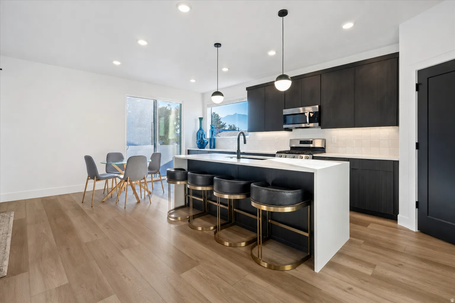 Kitchen featuring dark flat-panel cabinetry, stainless steel appliances, a white subway tile backsplash, and a large island with a white countertop