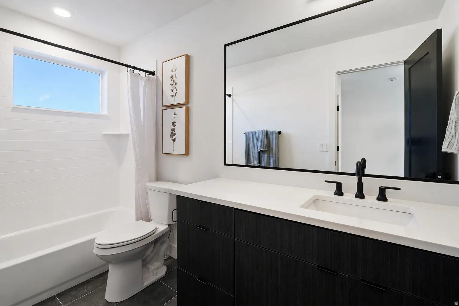 Sleek bathroom featuring a dark wood-finish vanity with a white countertop and integrated sink, matte black fixtures, and a large wall-mounted mirror