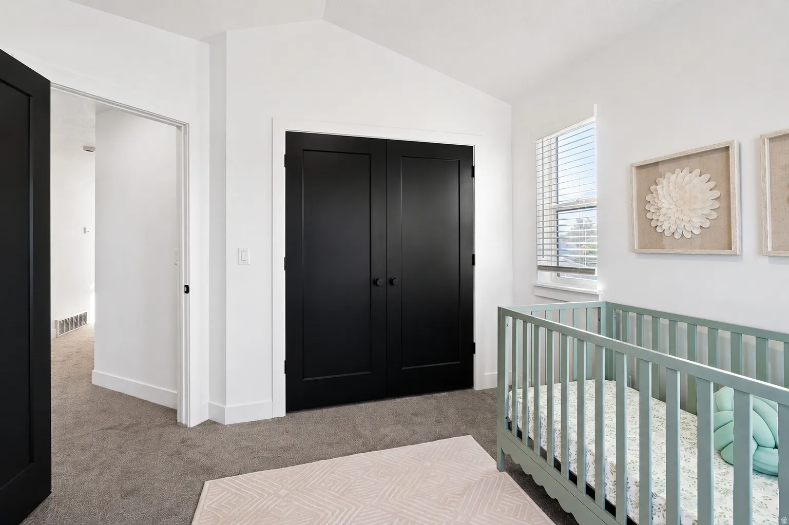 White walls with vaulted ceiling, dark panel doors, window with blinds, and gray carpet