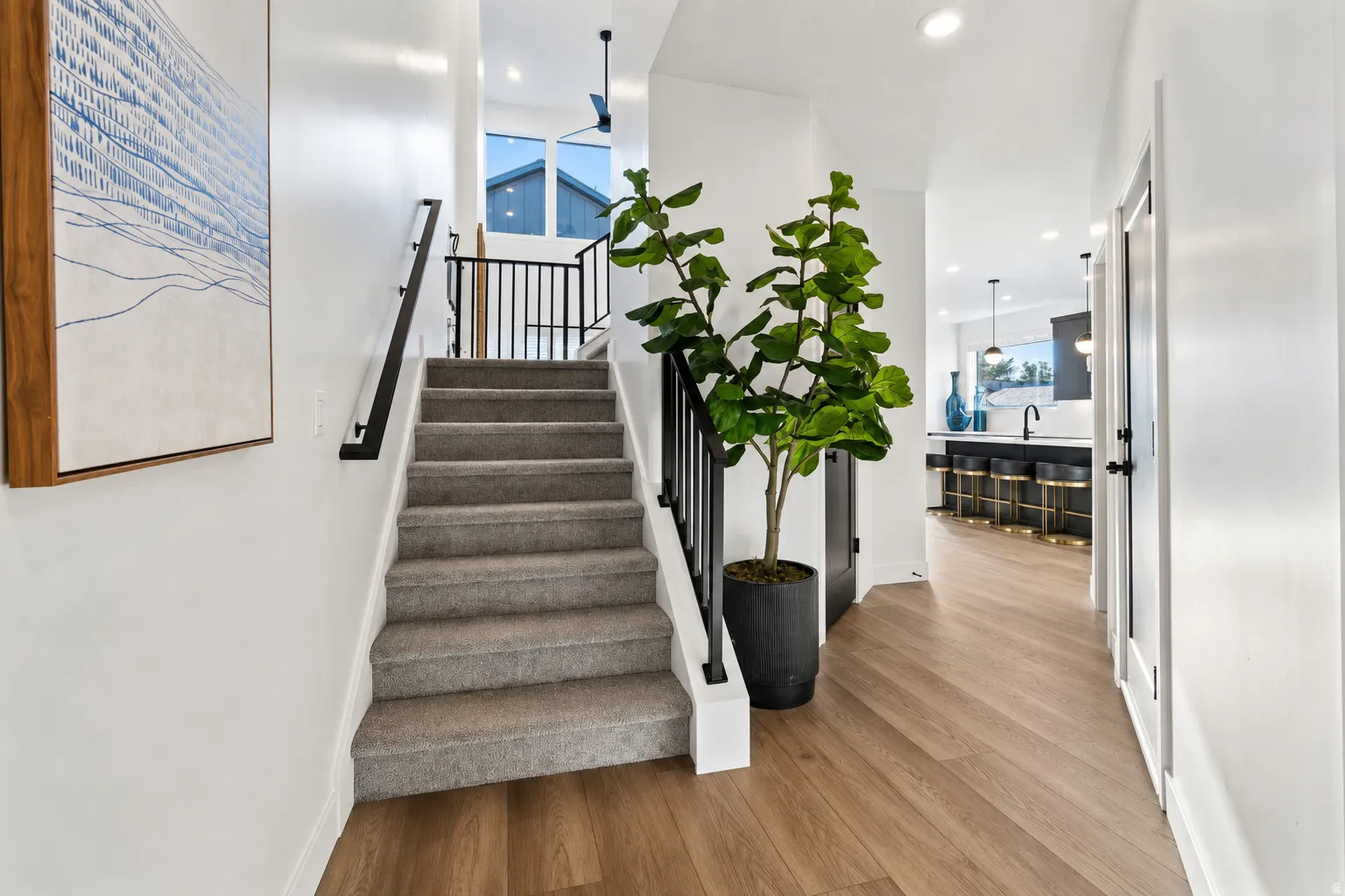 Hardwood-finish flooring, carpeted staircase with black railing, recessed lighting, and white walls