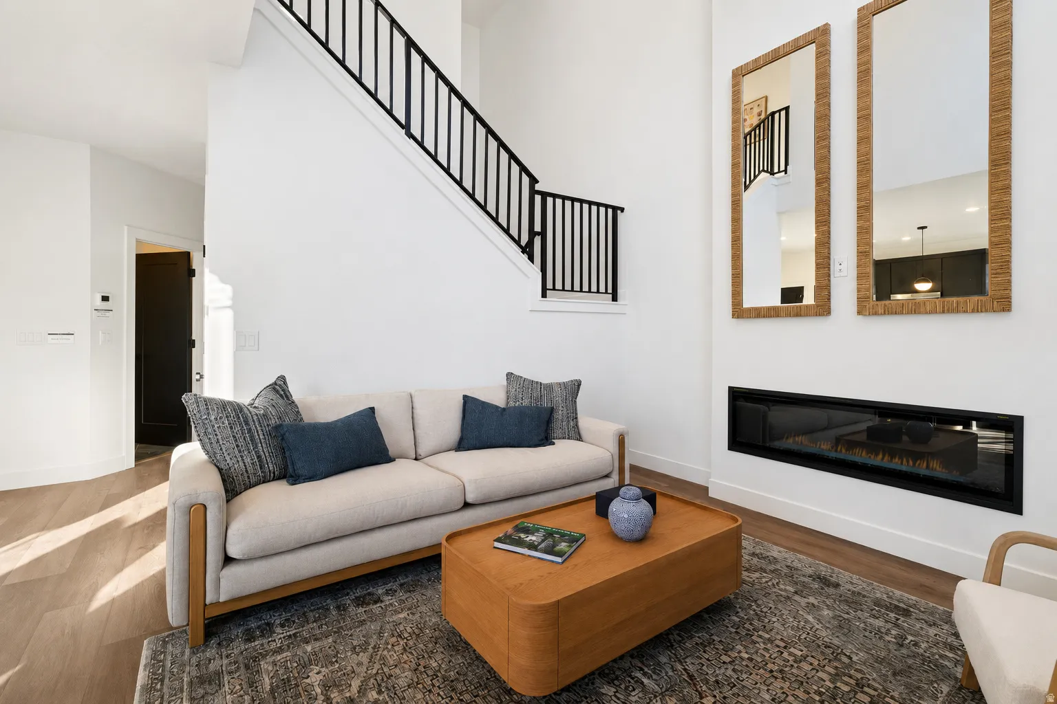 Wood-finish flooring, white walls, black metal staircase railing, and an elongated built-in fireplace