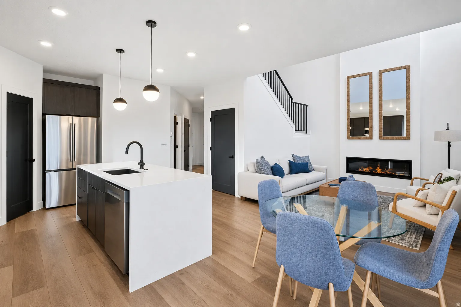 Open-concept living area featuring wood-finish flooring, a contemporary fireplace, and a kitchen island with an undermount sink