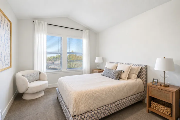 Vaulted ceiling with an accent wall, two large windows with blinds, and carpeted flooring