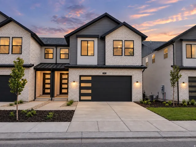 Modern duplex exterior featuring brick and siding, a two-car garage with contemporary doors, and multiple windows with black trim