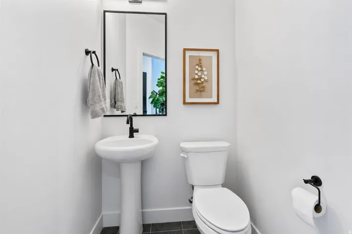 Pedestal sink with a matte black faucet, rectangular mirror with a black frame, and dark tile flooring