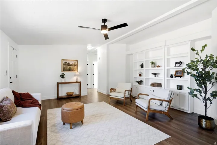 Bright living area featuring wood-finish flooring, a contemporary ceiling fan, and extensive built-in white shelving with lower cabinetry