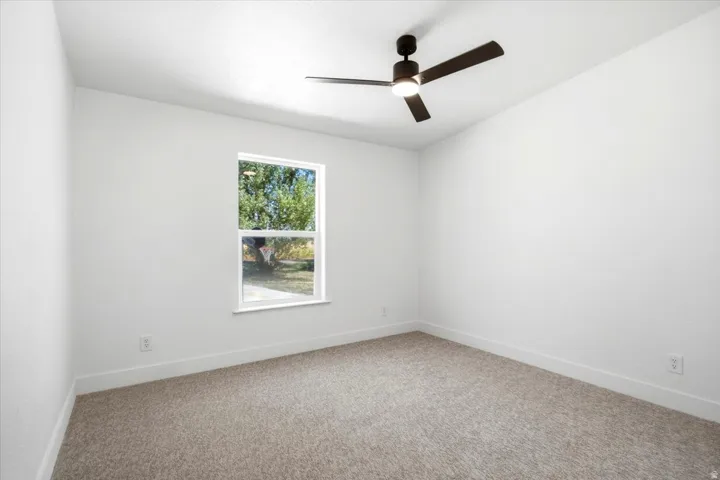 Neutral color palette with textured carpeting, a white-framed window, and a contemporary ceiling fan