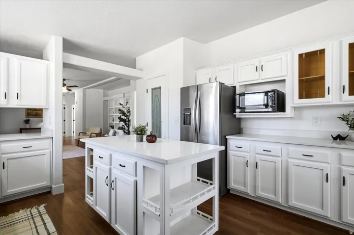 White cabinetry with dark hardware, stainless steel refrigerator, built-in microwave, white countertops, and wood-finish flooring