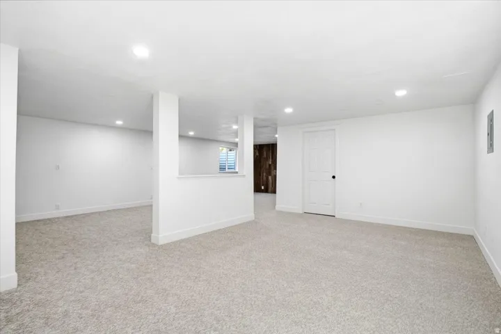 Recessed lighting illuminates the expansive carpeted flooring, featuring a half-wall partition and a solid core door