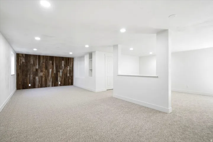 Recessed lighting, wood-panel accent wall, built-in shelving, light-toned carpet, and a half-wall partition