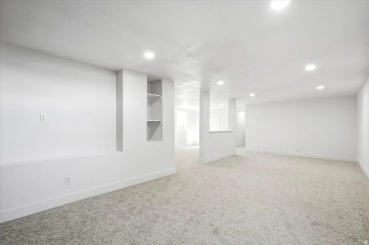 Recessed lighting illuminates a spacious room featuring light-colored carpeting, white walls, and built-in shelving