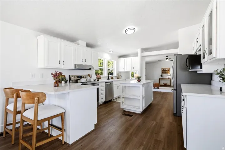 Kitchen featuring white cabinetry, stainless steel appliances, wood-finish flooring, a kitchen island, and white countertops
