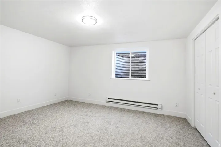 Recessed window, white window frame, baseboard heating unit, light grey carpeting, and bi-fold closet doors