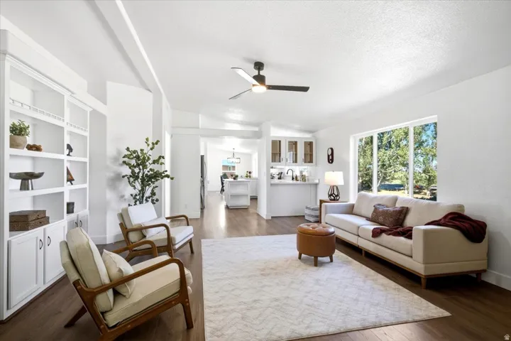 Open-concept living area featuring wood-finish flooring, built-in shelving, a ceiling fan, and large windows