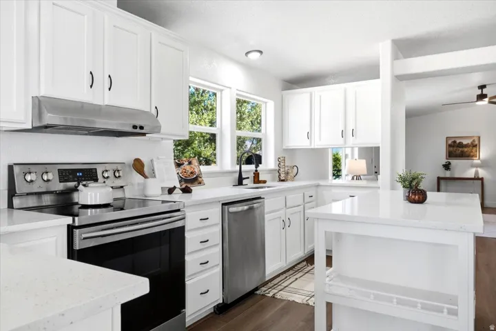 White shaker cabinetry, stainless steel appliances, white countertops, wood-finish flooring, and a kitchen island with built-in shelving