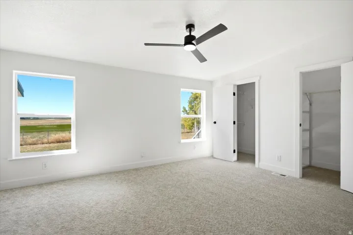 Neutral-toned carpeting, modern ceiling fan with integrated lighting, two windows, and two open closets with shelving