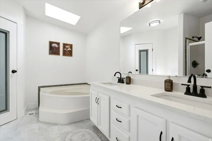 Bathroom featuring a dual vanity with white cabinetry, light-toned countertops, and matte black fixtures