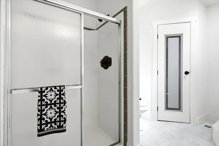 Frosted glass shower enclosure with bronze-finish fixtures, white wall tile, and light-toned floor tile