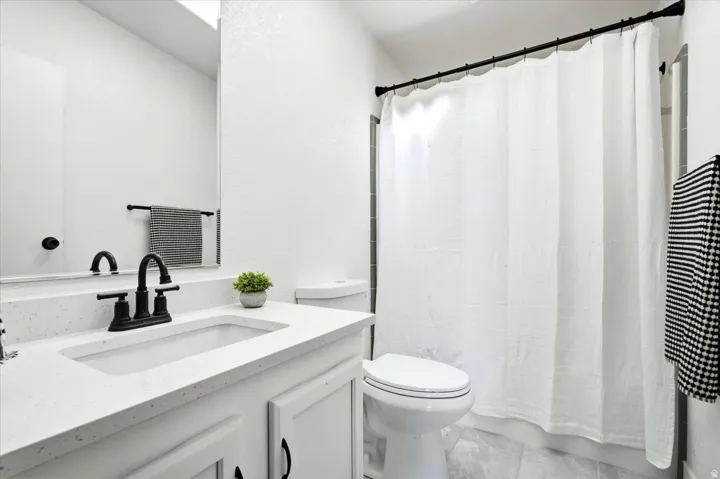 White vanity with a rectangular undermount sink, solid surface countertop, and matte black faucet