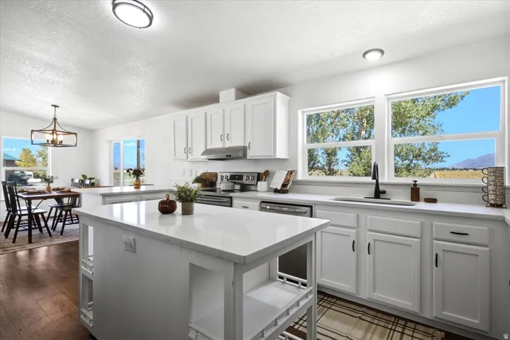 Kitchen featuring white cabinetry, light-toned countertops, a central island, stainless steel appliances, and wood-finish flooring