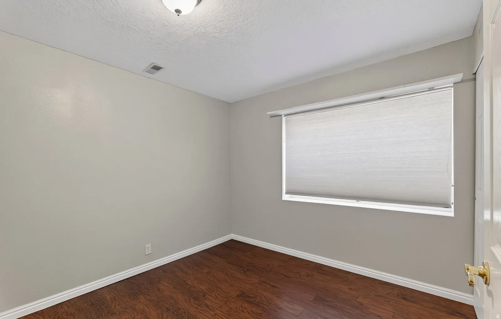 Wood-finish flooring with white baseboards, neutral wall paint, and a window featuring a roller shade